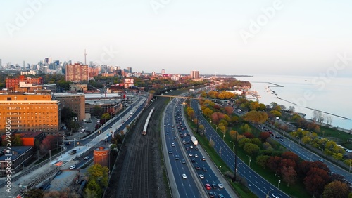 Top view of approaching train and highway traffic jam at sunset. Wide view of skyscrapers  green trees  calming lake and cars that are stuck in traffic jam. Leave early to avoid traffic jam on road.