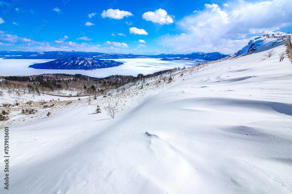爽快な青空と雪に覆われた斜面と眼下の氷に覆われた湖。爽やかな印象の冬景色。北海道の美幌峠から見下ろす屈斜路湖。 爽快な青空と雪に覆われた斜面と眼下の氷に覆われた湖。爽やかな印象の冬景色。北海道の美幌峠から見下ろす屈斜路湖。