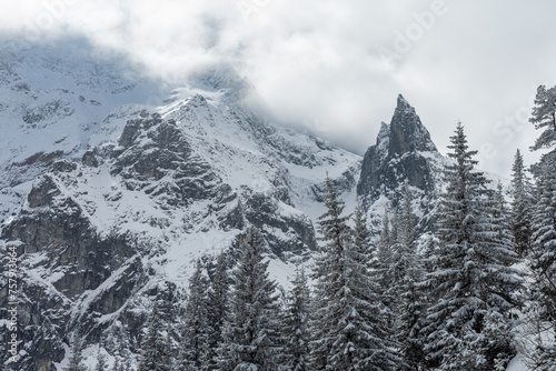 Polish Tatra mountains in winter with snowy trees and frozen Mnich (Monk) rocky mountain near morskie oko lake without people. High mountains covered with clouds. photo