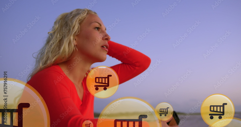 Obraz premium Image of shopping icons over midsection of caucasian woman using smartphone at beach