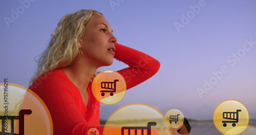 Image of shopping icons over midsection of caucasian woman using smartphone at beach
