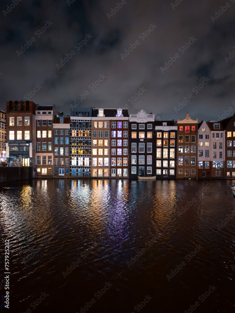 Traditional Dutch construction buildings on Damrak canal at night in Amsterdam in winter