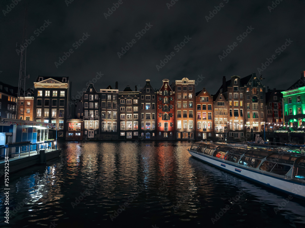 Traditional Dutch construction buildings on Damrak canal at night in Amsterdam in winter