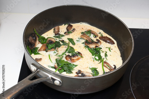 A spinach and mushroom omelette being cooked in a frying pan