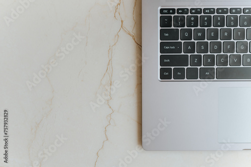 Modern metallic laptop top with black keyboard on marble table, cropped top view