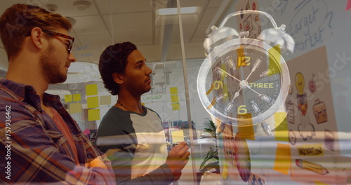 Image of clock over diverse businessmen taking notes