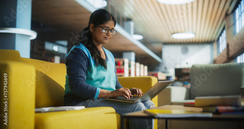 Smart Indian Female Student in Glasses Working on Software Development Assignment in a Quiet Public Library. Young South Asian Woman Using Laptop Computer and Preparing for Examination in College photo