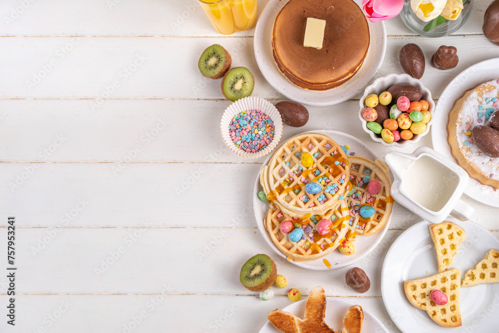 Easter holiday sweet breakfast, brunch. Easter decorated belgian waffles, pancakes, breakfast cereals and milk, fried eggs with toasts and bacon, Easter chocolate eggs and bunny, with spring flowers
