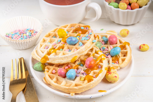 Easter breakfast or brunch. Cute creative decor portion of soft sweet belgian waffles with Easter chocolate eggs, sugar sprinkles and jam or syrup drizzles