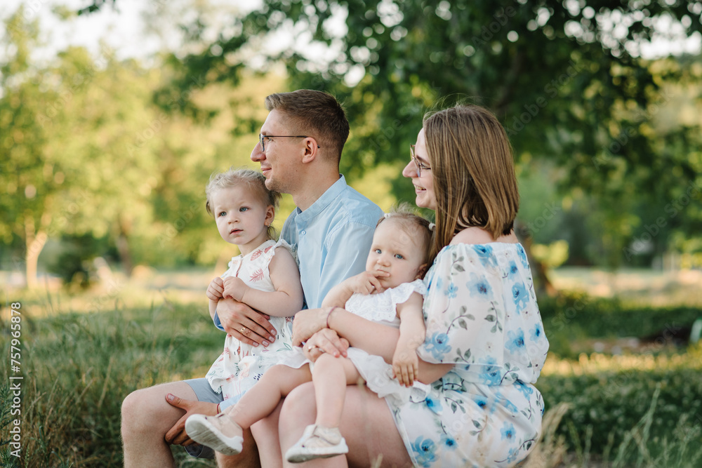 A happy family is sitting on bench on shore of lake at sunset. Mom, dad hug children daughter in the summer park. A loving couple with two childs. Mother, father embrace kids and spend time together. A happy family is sitting on bench on shore of lake at sunset. Mom, dad hug children daughter in the summer park. A loving couple with two childs. Mother, father embrace kids and spend time together.