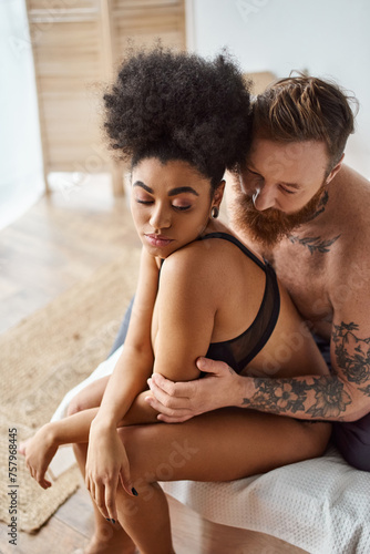 diverse couple, bearded man with tattoos and african american woman sharing a tender moment on bed