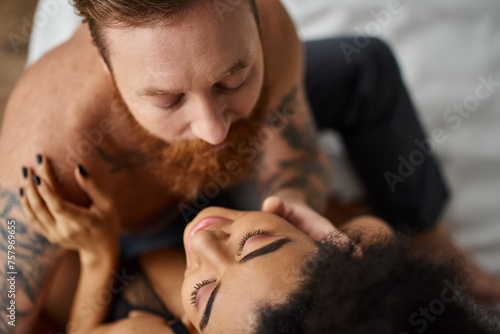 top view of bearded tattooed man embracing african american girlfriend in bra, diverse sexy couple