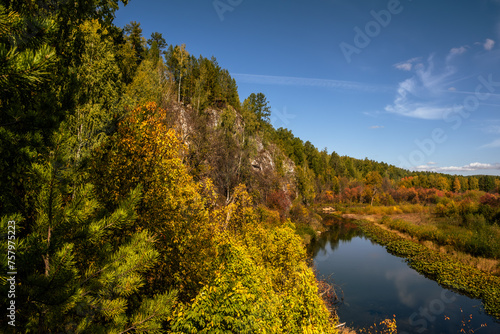 The river flows near the rocks covered with autumn forest.