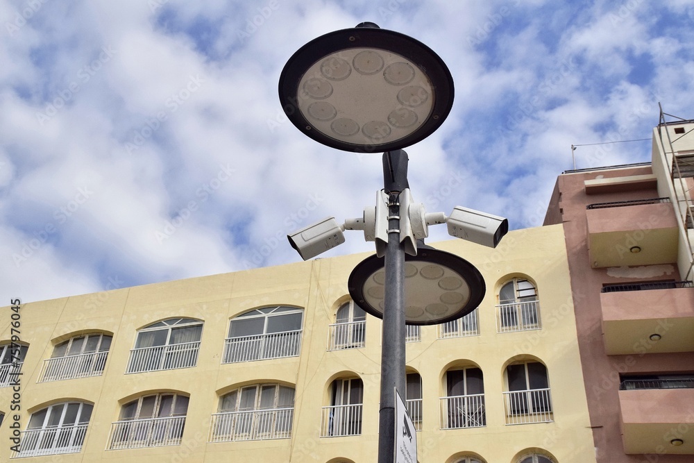 Surveillance cameras and round lights against the sky.  Copy space