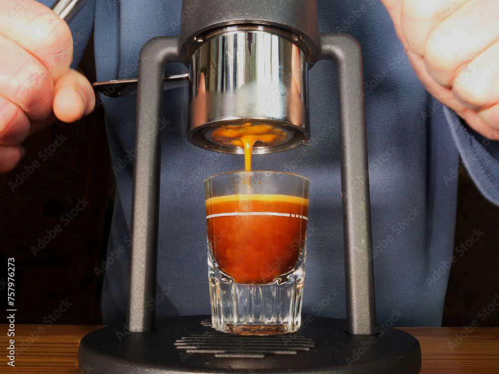 A man’s hands pushing down on the twin levers of a manual coffee machine, to deliver an espresso with crema foam into a shot glass. A man’s hands pushing down on the twin levers of a manual coffee machine, to deliver an espresso with crema foam into a shot glass.