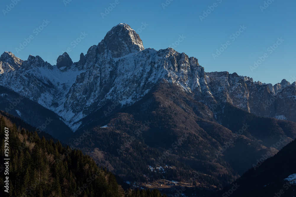 visuale in primo piano, del lato in ombra di una grande catena montuosa, in un ambiente naturale di montagna, parzialmente innevato, nelle alpi carniche nel nord-est Italia, al tramonto, in inverno