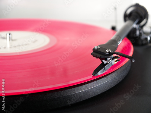 Closeup of a pink vinyl LP record on a turntable, with the tonearm needle or stylus positioned at the start of the first music track on one side of the album, ready to play.