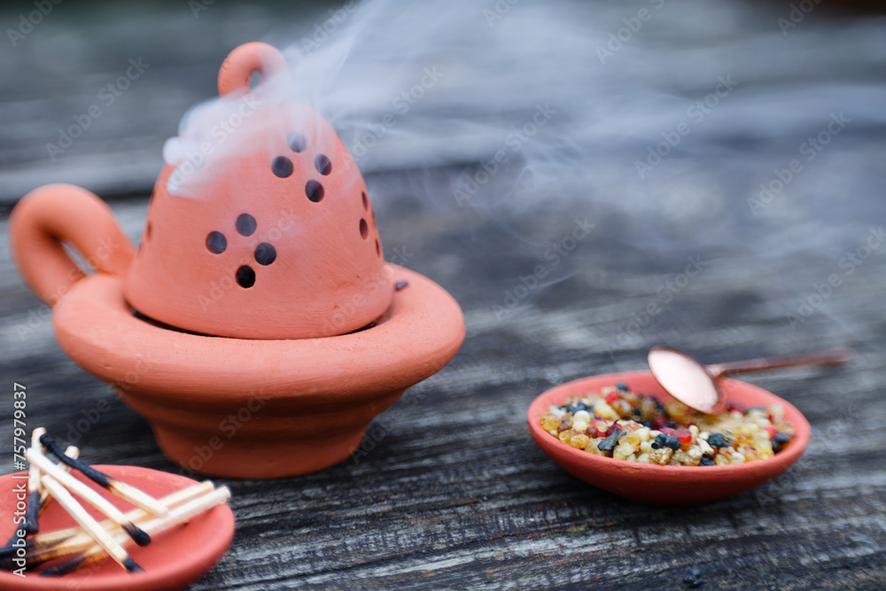 Fototapeta premium Clay simple censer (closed) with burning resin incense at the table outdoors. Burning smoke.