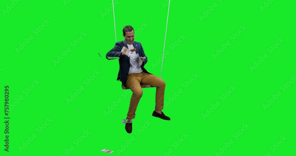 Happy man scattering euro cash sitting on rope swing against green background, Slow motion