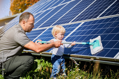 Father showing his little son the solar panels during sunny day. Cute boy helping his dad to clean solar battery. Young man teaching his small kid how to care about their source of energy.