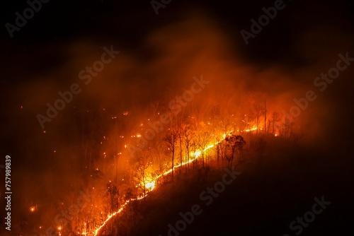 Orange forest fire rages in the mountains at night in Chiang Mai. It causes enormous amounts of toxic dust and smoke. Fires continue to burn, destroying forests and wildlife during the summer. photo