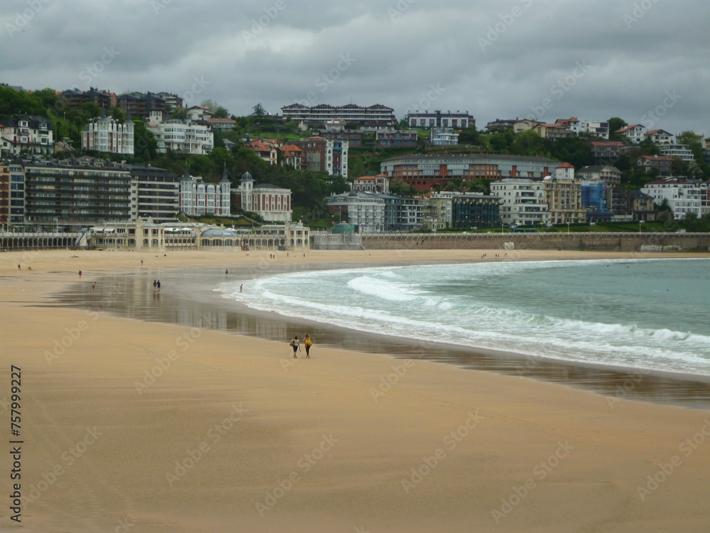 Fototapeta premium Beach landscape of the city of San Sebastián, País Vasco, Euskadi. Spain. Donostia. Tourists walking on the beach on a cloudy day.