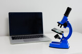 Computer with blank screen and blue microscope on white table with copyspace
