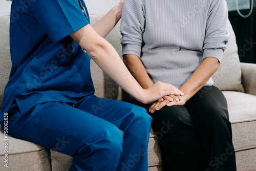 Young nurse helping elderly woman walk in the room, holding his hand, supporting. Treatment and rehabilitation after injury in assisted living facility.