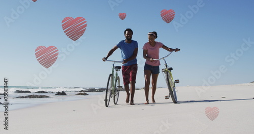 Image of hearts over happy african american couple walking with bikes on beach