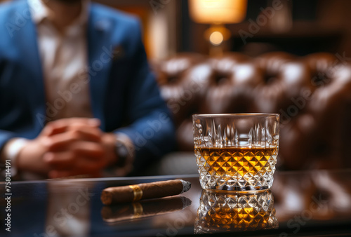 Whiskey and cigar  Glass with whiskey and a cigar on the table with a handsome man in a cigar smokers lounge.