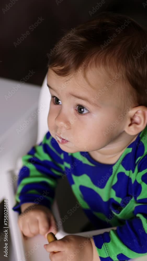 Adorable toddler eating porridge given by his mom on spoon. Lovely boy looking up while chewing. High angle view. Vertical video. Adorable toddler eating porridge given by his mom on spoon. Lovely boy looking up while chewing. High angle view. Vertical video.