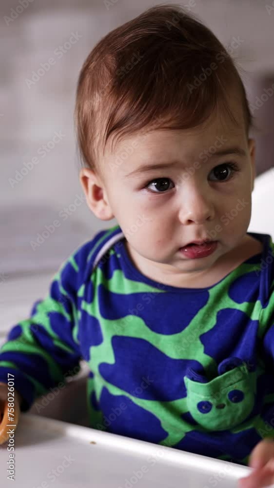 Lovely active baby boy in green spotted shirt sits at the dining table. Little kid waving hands and then stares at something. Close up. Vertical video. Lovely active baby boy in green spotted shirt sits at the dining table. Little kid waving hands and then stares at something. Close up. Vertical video.