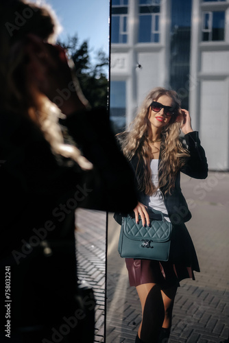 Portrait of fashionable young woman in black jacket walking by glass building