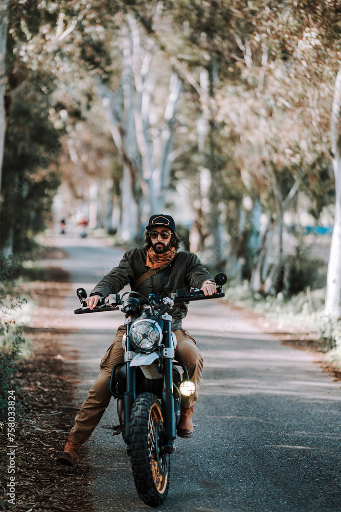 Chico con barba con atuendo de motorista posando con su moto y su cámara Chico con barba con atuendo de motorista posando con su moto y su cámara