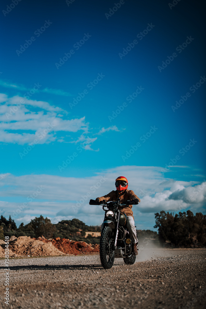 Obraz premium Motero en moto tipo scrambler por camino con arboles en la naturaleza
