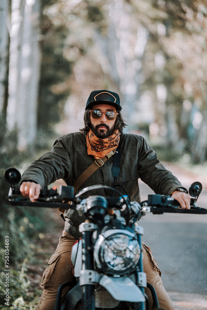 Chico con barba con atuendo de motorista posando con su moto y su cámara Chico con barba con atuendo de motorista posando con su moto y su cámara