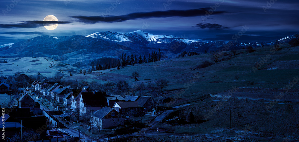 alpine countryside ant night. village in the valley and distant mountain range with snow capped tops in full moon light
