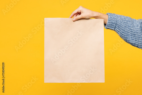 Close up cropped female holding in hand hold brown clear paper takeaway bag isolated on pastel plain yellow background. Food products delivery courier service concept. Copy space advertising mock up.