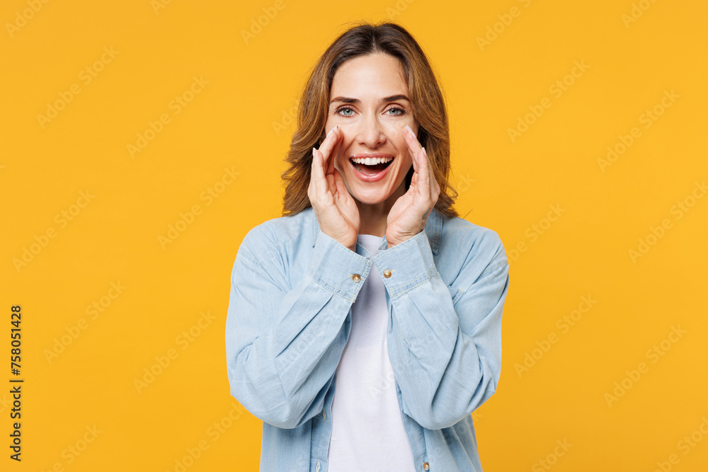 Young woman she wear blue shirt white t-shirt casual clothes scream sharing hot news about sales discount with hands near mouth isolated on plain yellow background studio portrait. Lifestyle concept. Young woman she wear blue shirt white t-shirt casual clothes scream sharing hot news about sales discount with hands near mouth isolated on plain yellow background studio portrait. Lifestyle concept.