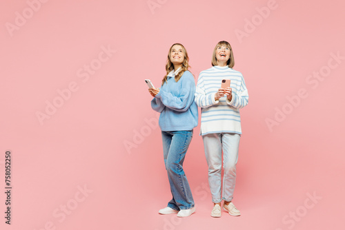 Full body elder parent mom young adult daughter two women together wear blue casual clothes hold use mobile cell phone look overhead isolated on plain pastel light pink background. Family day concept.