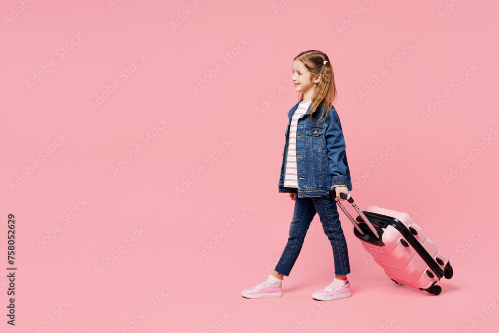 Traveler little child kid girl wears denim shirt wear casual clothes hold bag isolated on plain pink background. Tourist travel abroad in free spare time rest getaway. Air flight trip journey concept.