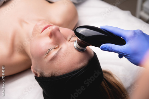Young woman undergoing facial rejuvenation procedure with tekar therapy in salon, top side view, close-up