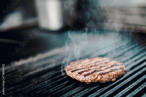 Fotografia A sizzling burger patty cooks on a grill, smoke rising from its perfectly seared surface