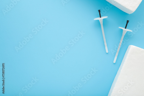 White insulation anchor dowels and styrofoam panels on blue table background. Closeup. Material for house thermal protection. Home facade repair work preparation. Empty place for text. Top down view. photo