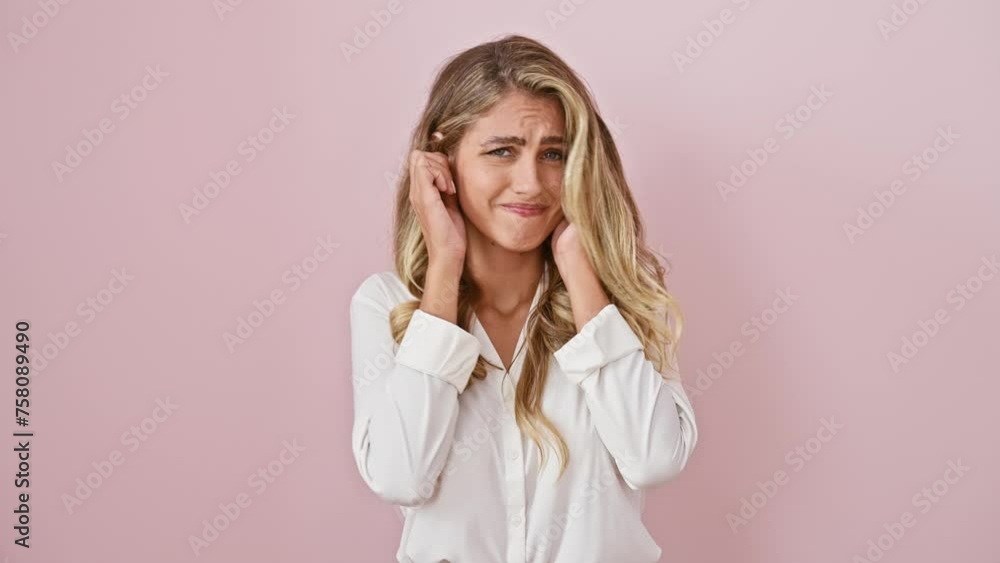 Annoyed young blonde woman in shirt covers ears with fingers over pink background, fed up with the noise of loud music Annoyed young blonde woman in shirt covers ears with fingers over pink background, fed up with the noise of loud music