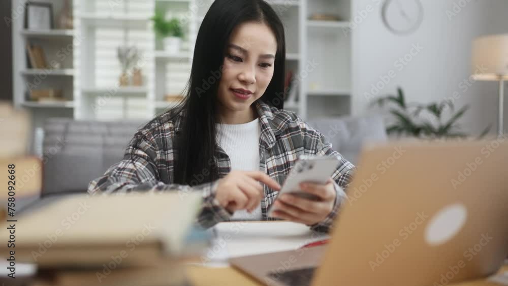 Positive young asian woman student or freelancer relaxing at home typing browsing products in internet online store reading news or social media profile on smartphone while take a break indoors Positive young asian woman student or freelancer relaxing at home typing browsing products in internet online store reading news or social media profile on smartphone while take a break indoors