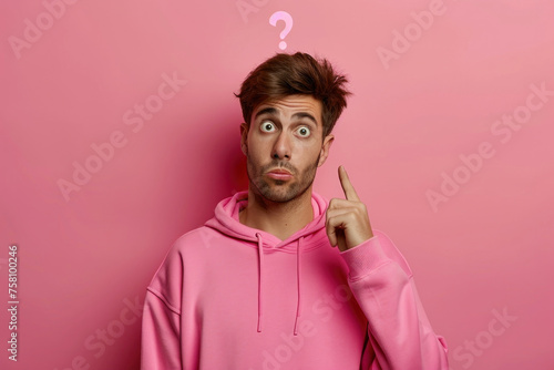 Curious man in a pink hoodie pointing up with a question mark on a pink background, wondering about something exciting