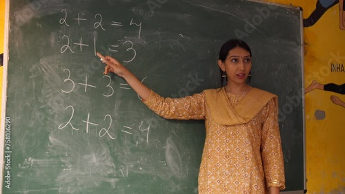 Young female Indian teacher teaching basic mathematics in class - maths  maths class  blackboard teaching. Government school teacher testing addition capabilities of her students - village school  ...