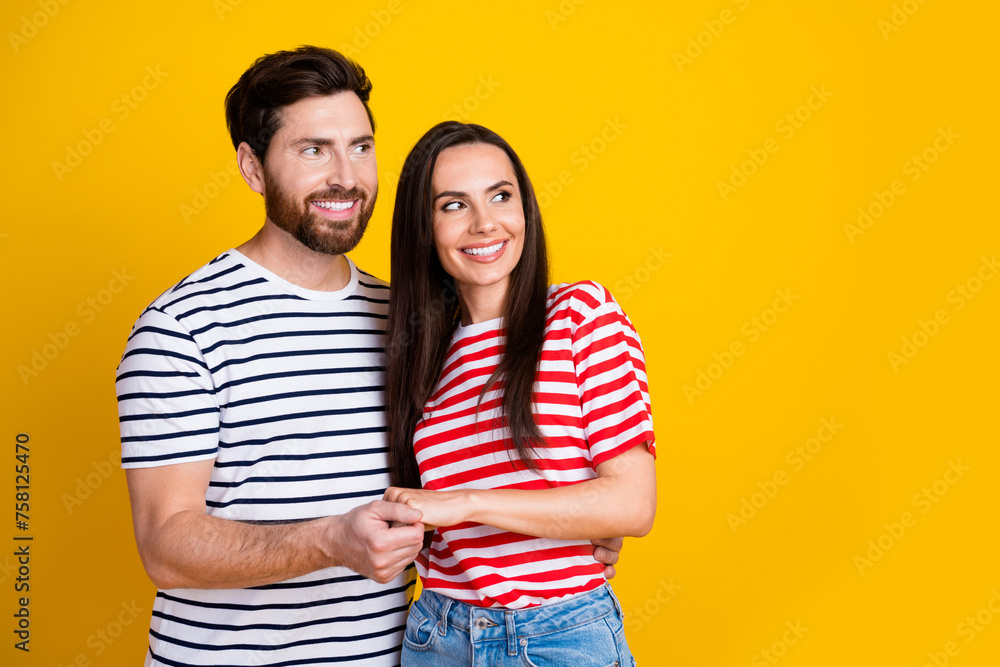 Photo portrait of attractive young couple hold hands look empty space wear trendy striped clothes isolated on yellow color background Photo portrait of attractive young couple hold hands look empty space wear trendy striped clothes isolated on yellow color background