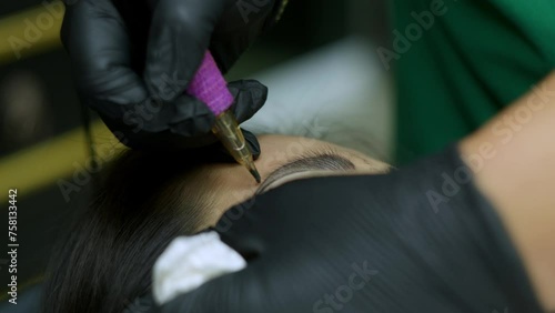 Close up microblading eyebrow tattoo. Beautician in gloves makes permanent makeup correction of the shape of the eyebrows to a young women. Eyebrow tattoo in a beauty salon. photo